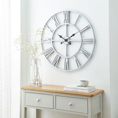 a large clock on the wall above a table with flowers in a vase and books