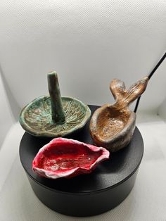 three ceramic birds sitting on top of a black stand next to a red bowl and spoon