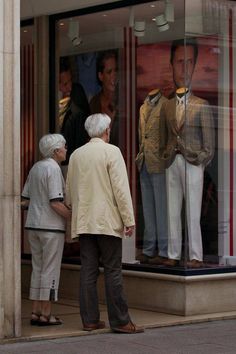 an elderly couple looking at mannequins in a store window with their reflection