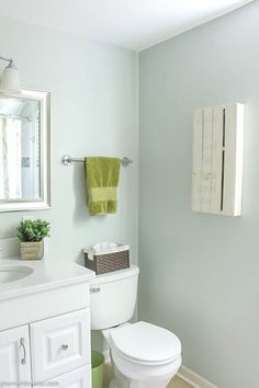 a white toilet sitting under a bathroom mirror next to a green towel hanging on the wall