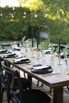 an outdoor dining table set up with black and white plates, silverware and candles