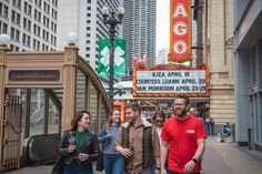 people walking down the street in front of a theater sign and buildings with signs on it