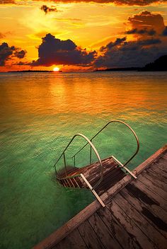 a boat sitting on top of a wooden dock in the ocean under a cloudy sky