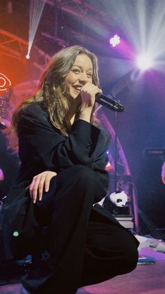 a woman sitting on top of a stage while holding a microphone in her right hand