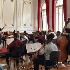 a group of people playing instruments in a room filled with red drapes and windows