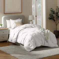 a white bed sitting in a bedroom on top of a wooden floor next to a window