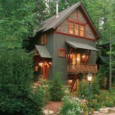 a house in the woods surrounded by trees and flowers with lights on at the front