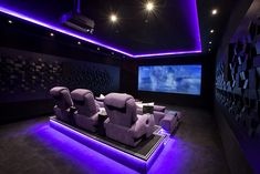 an empty theater room with purple lighting and recliners on the floor in front of a large screen