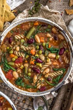 two bowls filled with pasta and vegetables next to crackers on the side, one bowl is full of soup