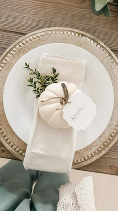 a place setting with white pumpkins, napkins and greenery on the table