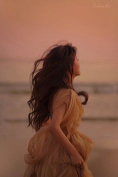 a woman in a dress is walking on the beach with her hair blowing in the wind