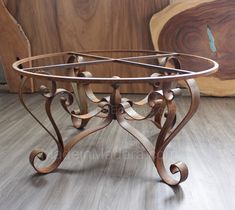 a wooden table with an iron frame and wood carvings on the top, sitting in front of a piece of wood