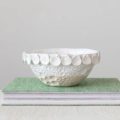 a white ceramic bowl sitting on top of a green book next to a stack of books