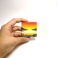 a hand holding up a small card with an image of a sunset in the background