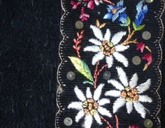 an embroidered piece of cloth with buttons and flowers on the side, sitting on a black surface