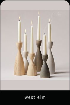 six candles are lined up in different shapes and sizes, with one lit candle between them