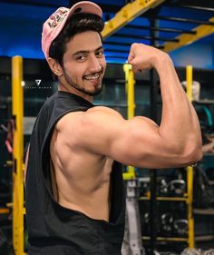 a young man flexing his muscles in the gym with a pink hat on top of his head