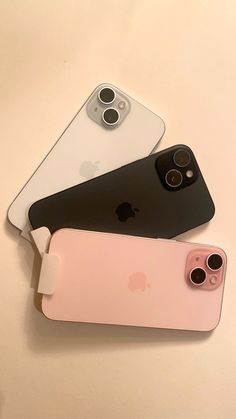 three iphones sitting next to each other on top of a white table with two black and one pink