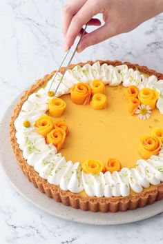 a person cutting into a cake with white frosting and orange flowers on it,