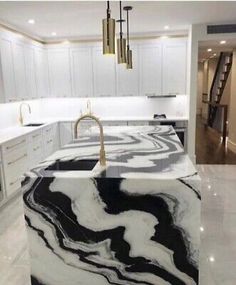 a marble counter top in a kitchen with white cabinets and gold faucet lights