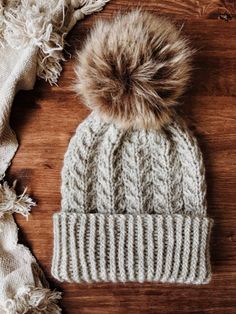 a white hat with a brown pom - pom sitting on top of a wooden table