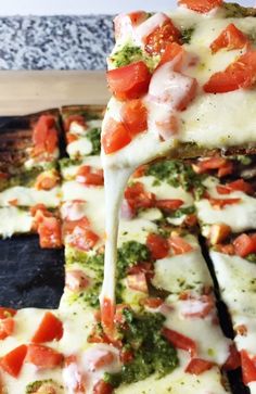 a pizza with tomatoes, broccoli and cheese being held by a spatula