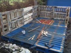 a wooden pallet sitting on top of rocks next to a blue building with tools in it