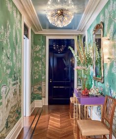 the hallway is decorated with green and blue wallpaper, gold chandelier, wooden chairs, and a purple table