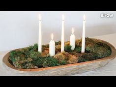 four white candles are placed in a moss covered bowl