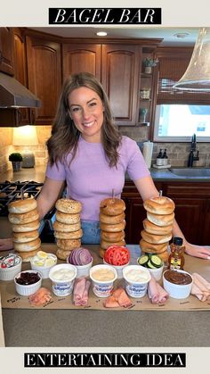 a woman standing in front of stacks of bagels and other food items on a counter