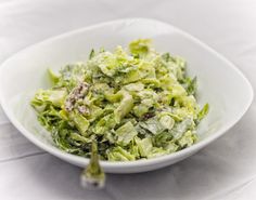 a white bowl filled with lettuce on top of a table next to a fork