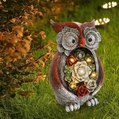 an owl figurine with flowers and lights on it's face sitting in the grass