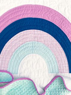 a close up of a quilt on a bed with the rainbow in the middle and pink, blue, and white circles