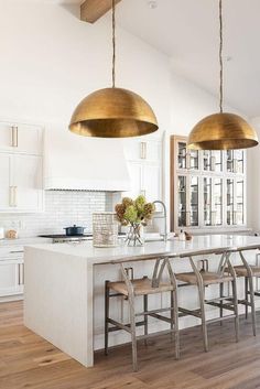 a kitchen with two pendant lights over the island and four stools in front of it