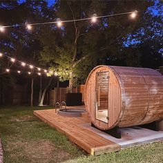 a wooden barrel sauna in the middle of a yard with string lights strung around it