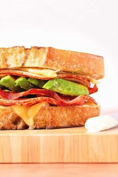 a sandwich with bacon, lettuce and cheese on it sitting on a cutting board