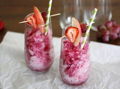 two glasses filled with ice and strawberries on top of a white cloth covered table