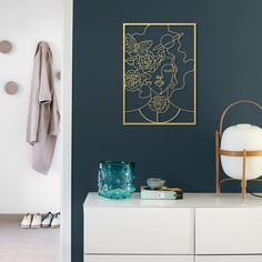 a white dresser with a blue wall and gold framed artwork on the wall next to it