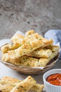 garlic bread sticks in a basket next to some dipping sauce on a white tablecloth