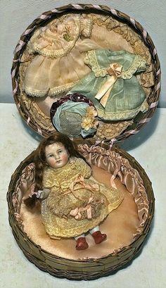 an old fashioned doll in a basket with two dolls inside it and one is laying on the floor