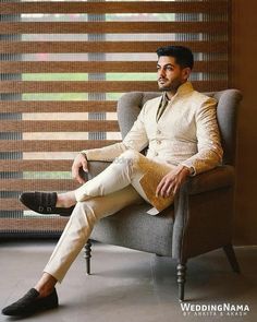 a man sitting in a chair with his legs crossed and wearing a white suit, black shoes