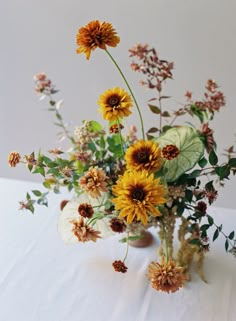 a vase filled with lots of flowers on top of a white table covered in leaves