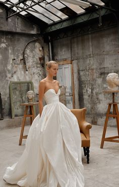 a woman in a white wedding dress standing next to a brown chair and an old building