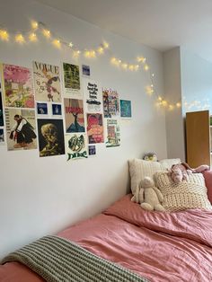 there is a bed with pink sheets and pictures on the wall next to it,