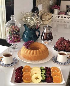 an assortment of fruits and pastries on a white table with a blue vase filled with flowers