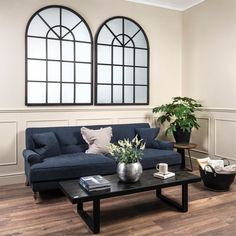 a living room with two large windows and a blue couch in front of the coffee table