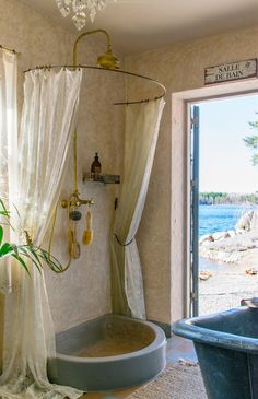 a bath tub sitting under a chandelier next to a bathroom window with an ocean view