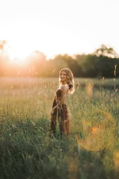 a woman standing in tall grass with the sun behind her