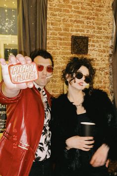 a man and woman pose for a photo in front of a brick wall holding up a candy bar