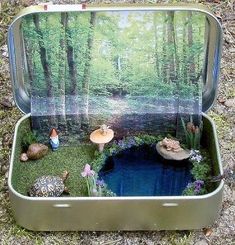 an open suitcase filled with miniature figurines in the grass and water surrounded by trees